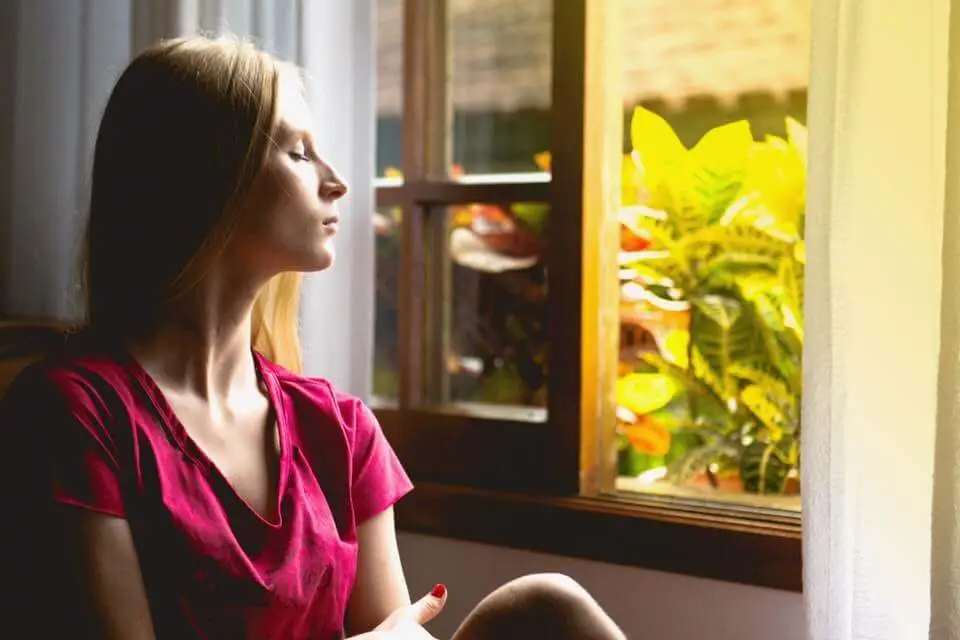 Blonde woman sitting with her eyes shut looking out the window with sun shining outside