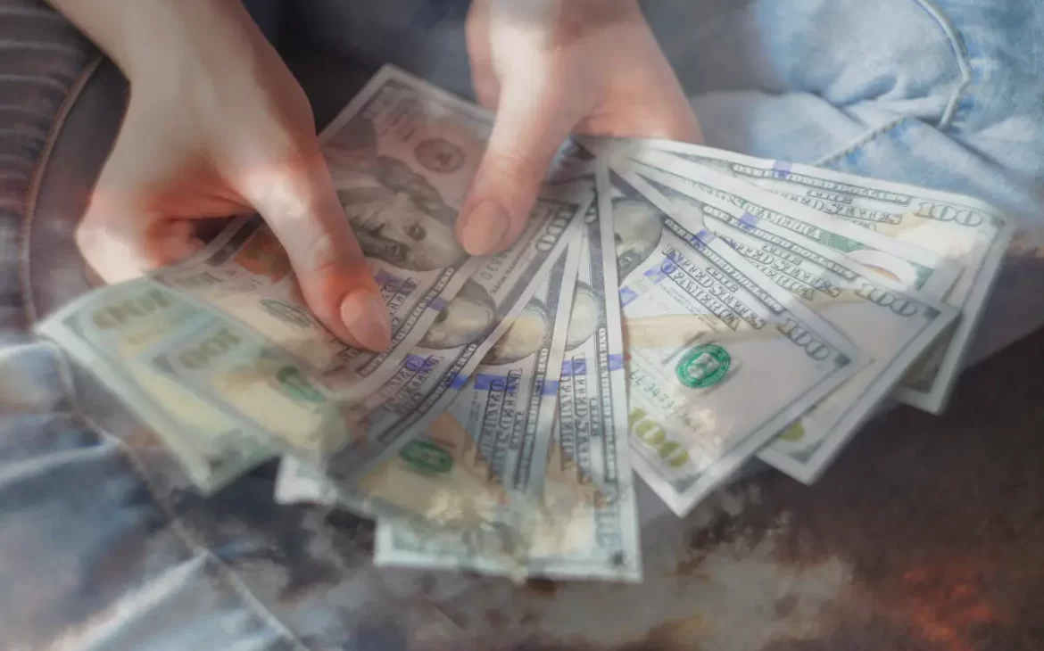 A woman holding a bunch of $100 bills, to demonstrate the importance of removing money blocks for more abundance