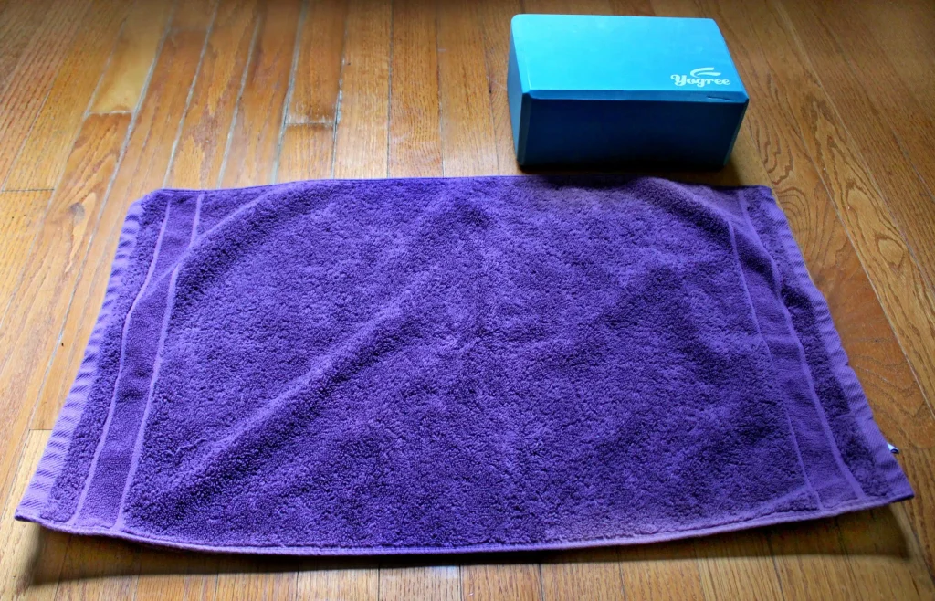 Folded purple hand towel next to a teal foam yoga block on a hardwood floor