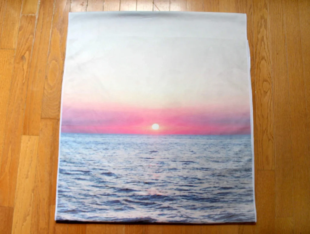 Yoga towel printed with a pink sunset over the ocean, ideal for what to bring to a hot yoga class